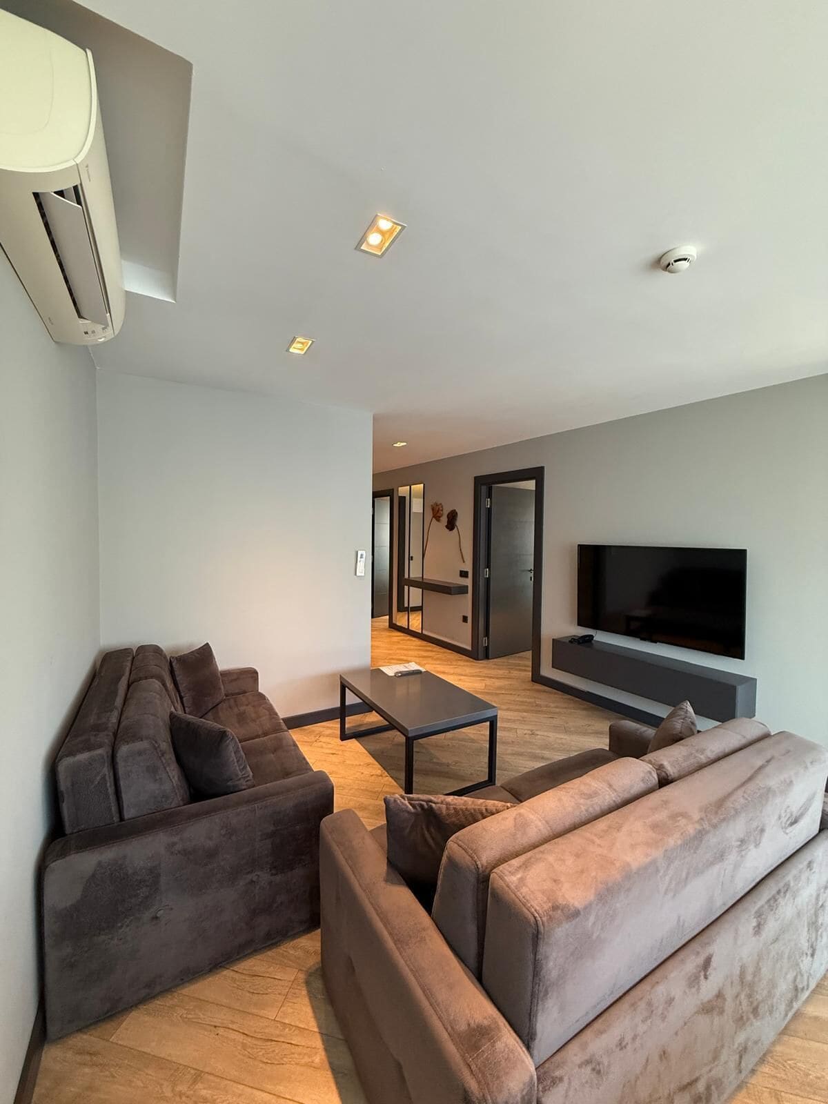 A modern living room with a sofa set, a coffee table, and a flat-screen TV mounted on the wall.