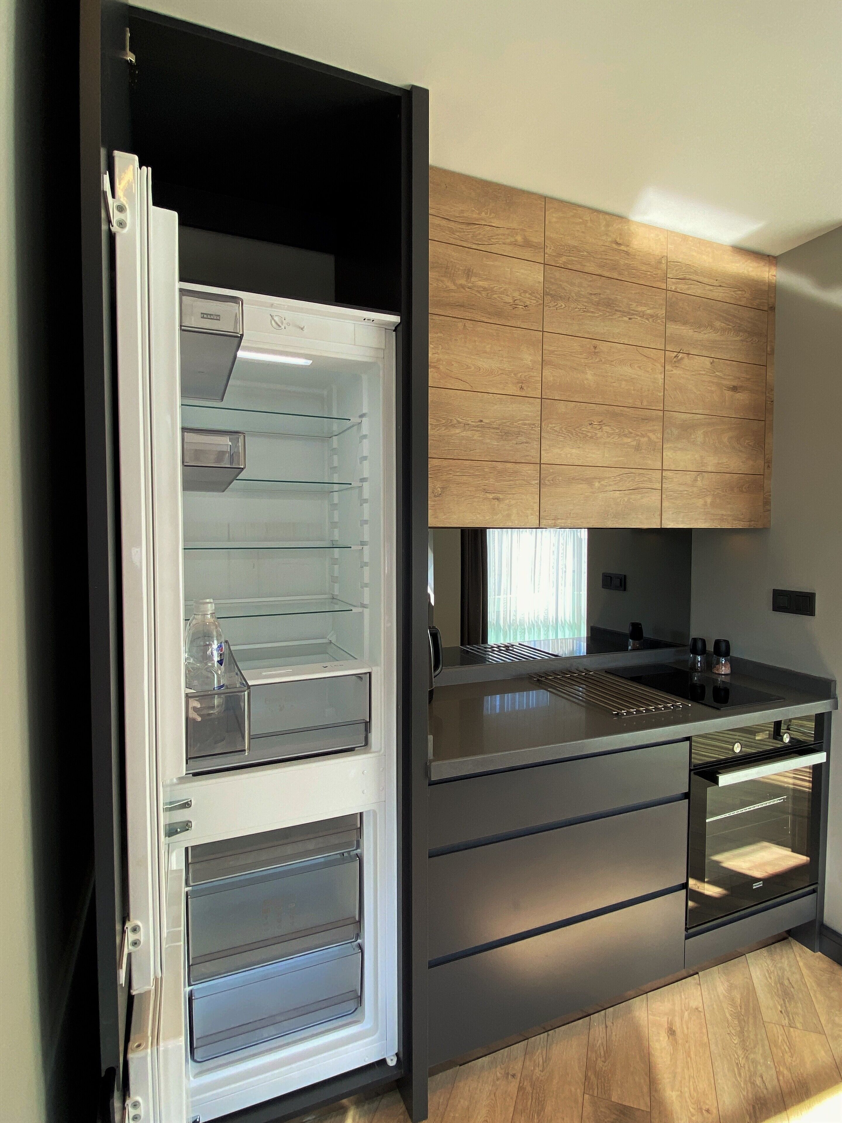 Cozinha moderna com geladeira embutida, armários de madeira e bancada de aço inoxidável.