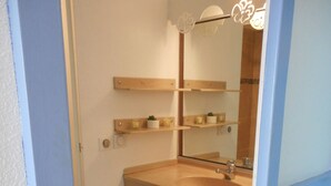 Ein Badezimmer mit Waschbecken, Spiegel, Handtuchhalter und einer kleinen Ablage mit Pflanze und Kerze.