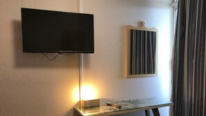 Ein Zimmer mit einem an der Wand befestigten Fernseher, einem Glastisch mit einer Lampe und einem gerahmten Kunstwerk.