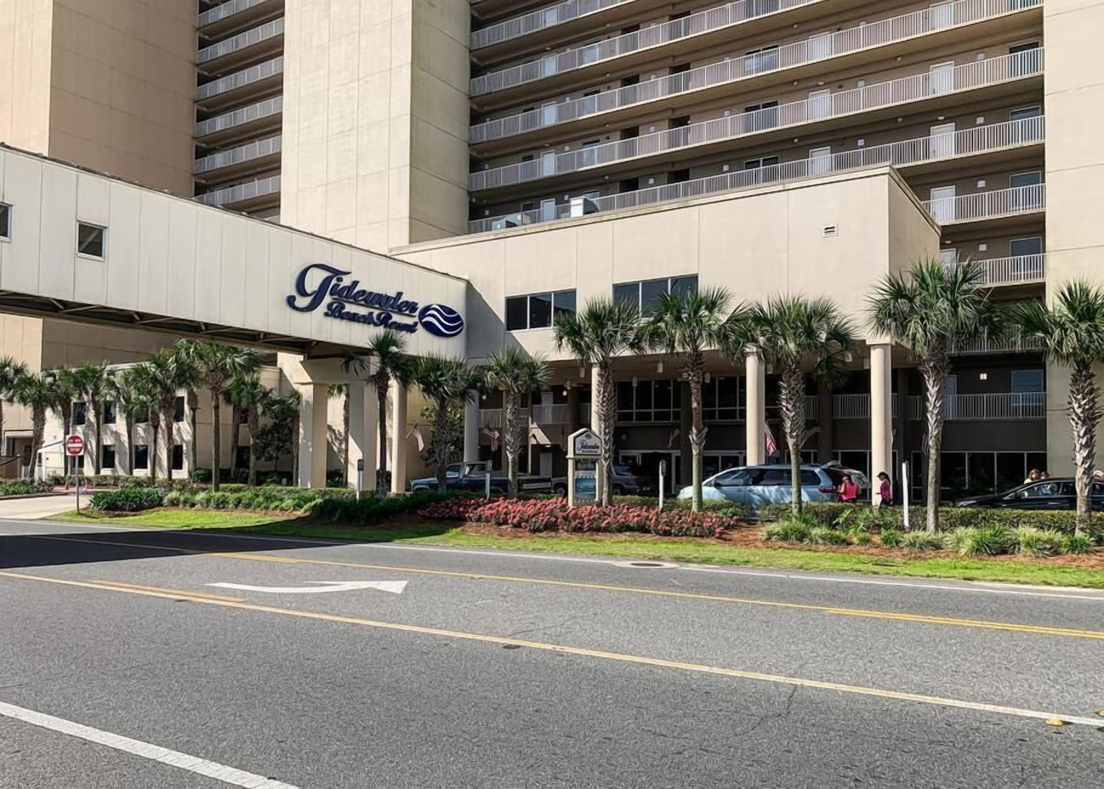A hotel with a large sign, multiple floors, and a parking lot.
