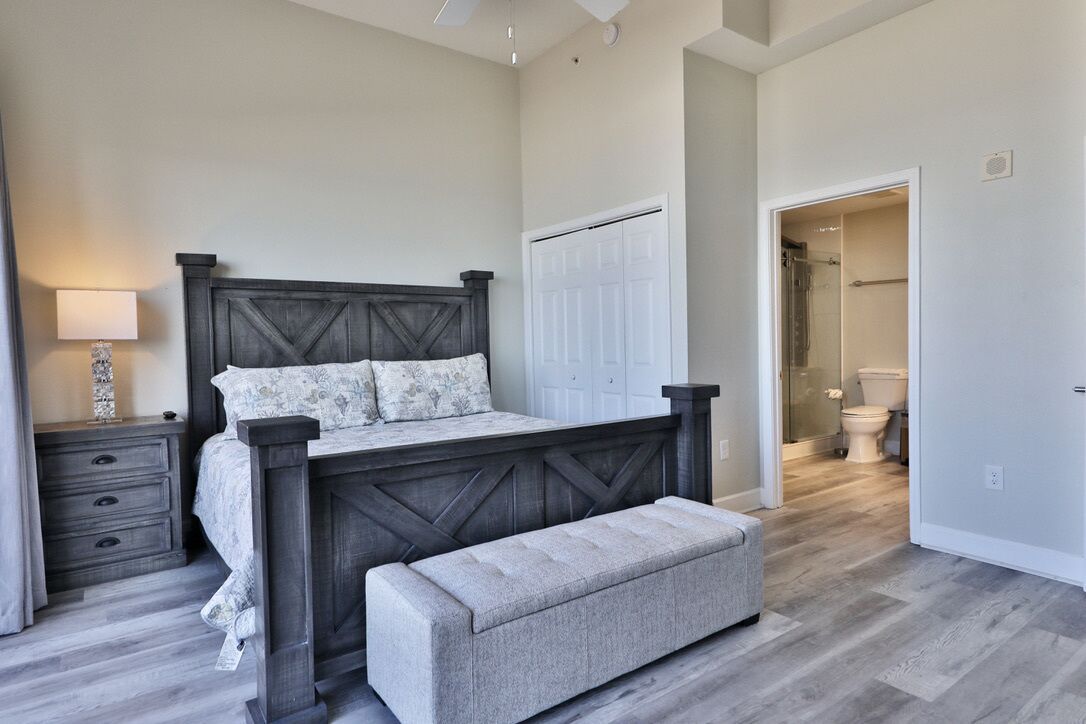 A bedroom with a bed, nightstand, bench, and a door leading to a bathroom.