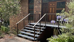 A brick building with a wooden door, a staircase with metal railings, and a garden with purple flowers. - A quiet comfortable space in the trees close to all the attractions of Denmark (Denmark)