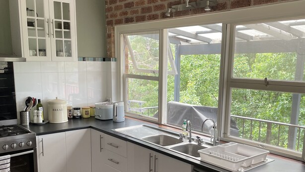 A modern kitchen with a brick wall, white cabinets, a stainless steel sink, and a view of greenery outside. - A quiet comfortable space in the trees close to all the attractions of Denmark (Denmark)