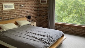 A bedroom with a brick wall, a bed with a wooden frame, a nightstand, a lamp, and a window with a view of trees. - A quiet comfortable space in the trees close to all the attractions of Denmark (Denmark)