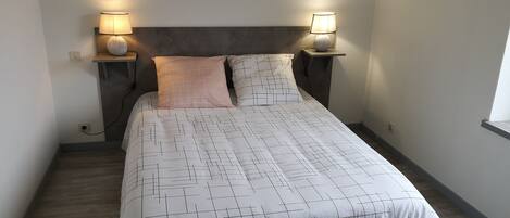 A neatly made bed with a geometric patterned bedspread, two bedside lamps, and a dark headboard.