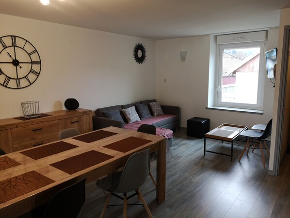 A modern living room with a wooden dining table, a sofa, and a TV.