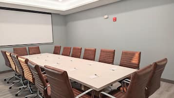 Ein Konferenzraum mit einem langen Tisch, braunen Ledersesseln, einer Projektionsleinwand und einem Rauchmelder.