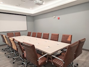 A conference room with a long table, brown leather chairs, a projector screen, and a fire alarm. - Candlewood Suites Tulsa Hills Jenks (Tulsa)