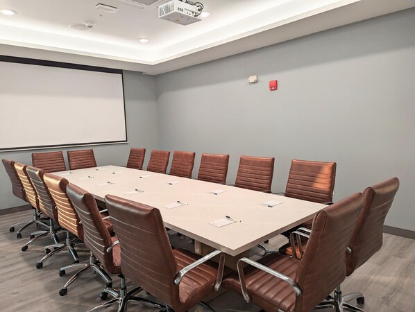 A conference room with a long table, brown leather chairs, a projector screen, and a fire alarm. - Candlewood Suites Tulsa Hills Jenks (Tulsa)