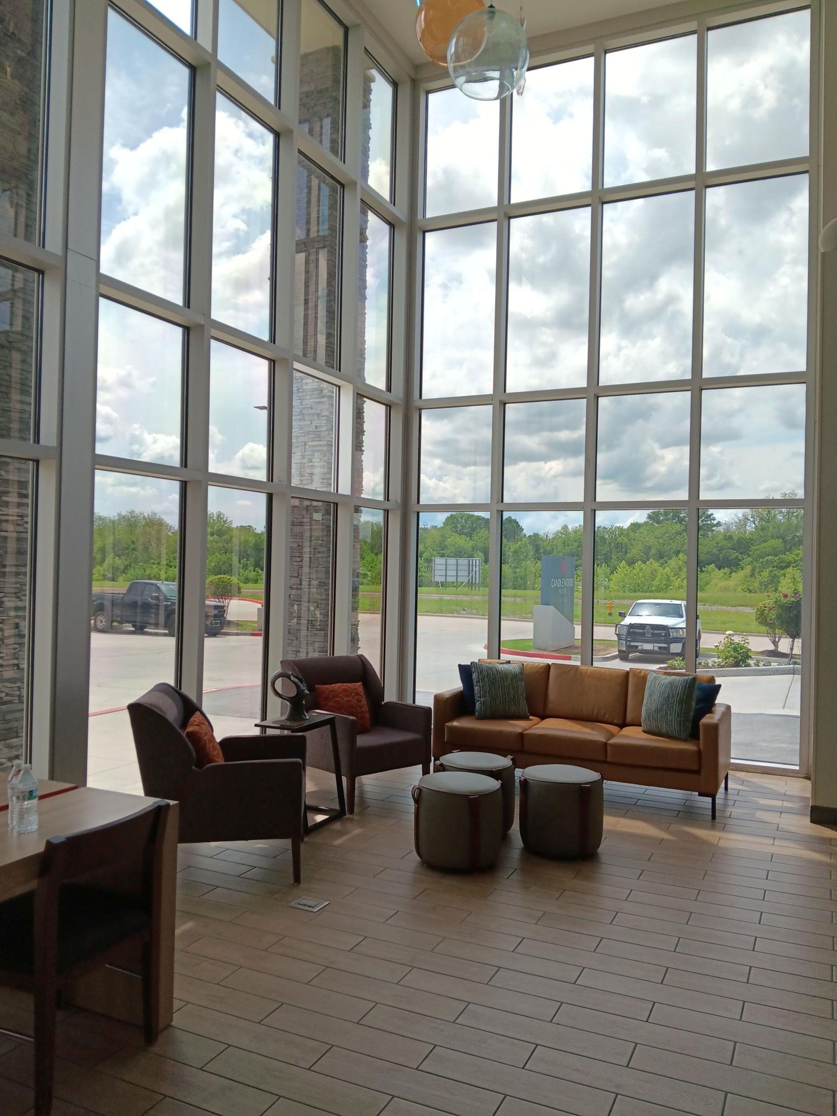 A spacious room with large windows, a brown leather sofa, a brown armchair, and a small table with a chair.