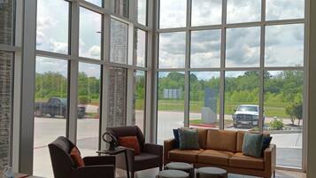 A spacious room with large windows, a brown leather sofa, a brown armchair, and a small table with a chair.