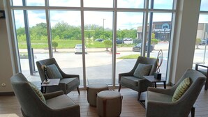 A spacious indoor area with large windows, comfortable seating, and a view of a parking lot and a building with a sign reading "FRONTIER JUST". - Candlewood Suites Tulsa Hills Jenks (Tulsa)