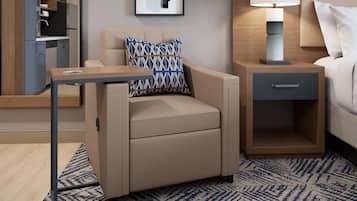A hotel room with a sofa, a side table, a nightstand, a lamp, and a patterned rug.