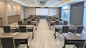 A conference room with a large screen, multiple tables, and chairs. - Candlewood Suites Tulsa Hills Jenks (Tulsa)