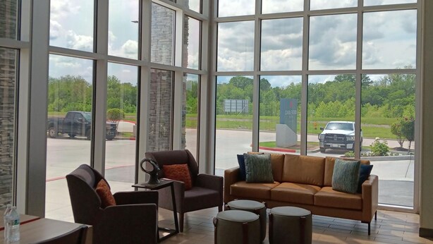 A spacious room with large windows, a brown leather sofa, a brown armchair, and a small table with a chair. - Candlewood Suites Tulsa Hills Jenks (Tulsa)