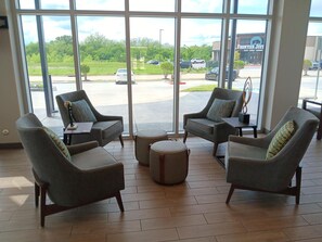 A spacious indoor area with large windows, comfortable seating, and a view of a parking lot and a building with a sign reading "FRONTIER JUST". - Candlewood Suites Tulsa Hills Jenks (Tulsa)