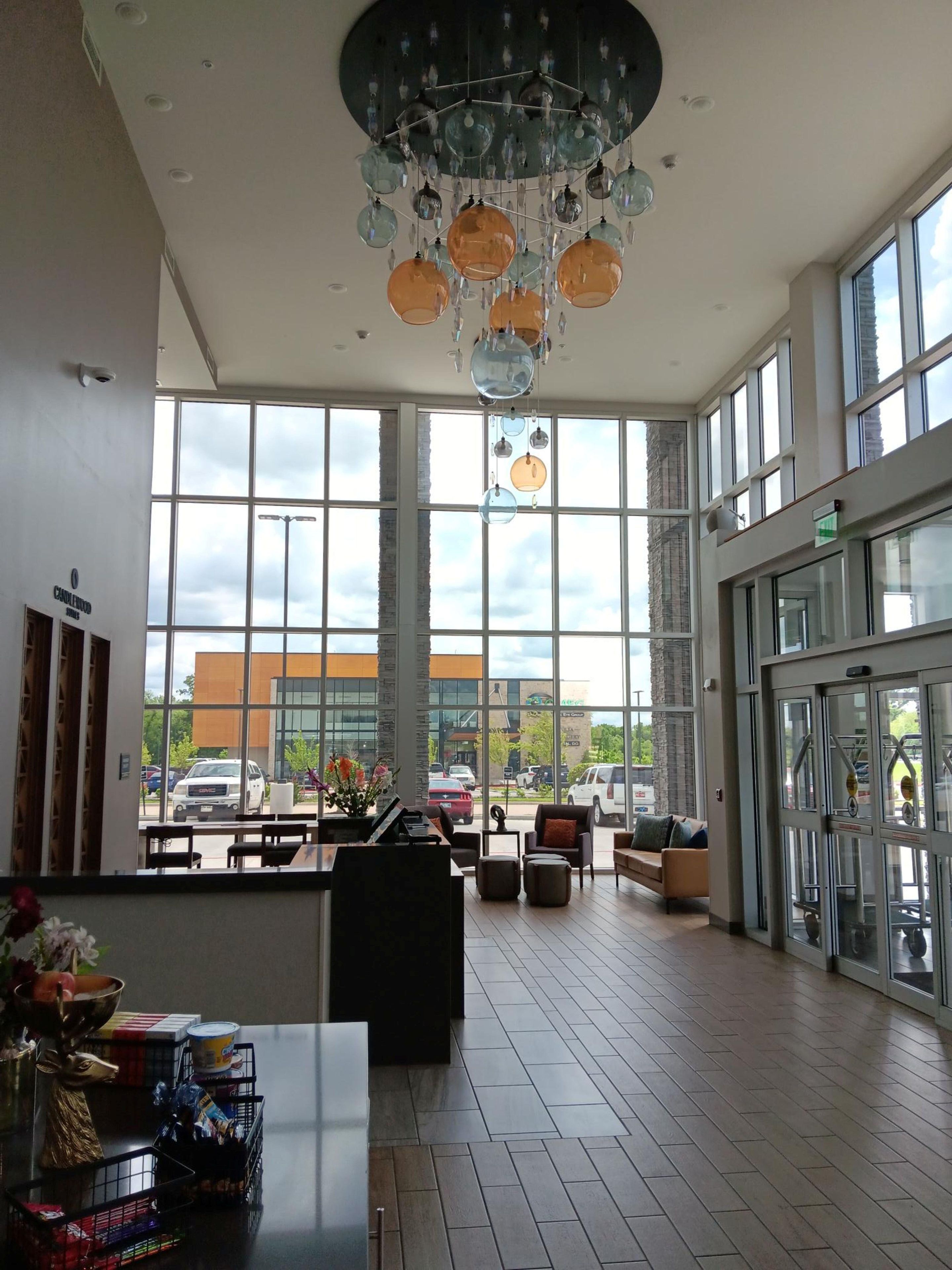 A spacious lobby with large windows, a piano, seating area, and a decorative chandelier.