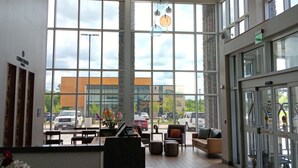 Um hall amplo com grandes janelas, um piano, área de estar e um lustre decorativo.