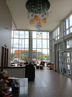 A spacious lobby with large windows, a piano, seating area, and a decorative chandelier. - Candlewood Suites Tulsa Hills Jenks (Tulsa)