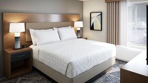 Quarto de hotel com uma cama grande, duas mesas de cabeceira com abajures, uma cabeceira, uma janela com cortinas e um quadro na parede.