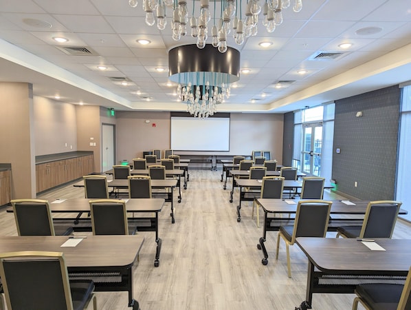 A conference room with a large screen, multiple tables, and chairs. - Candlewood Suites Tulsa Hills Jenks (Tulsa)