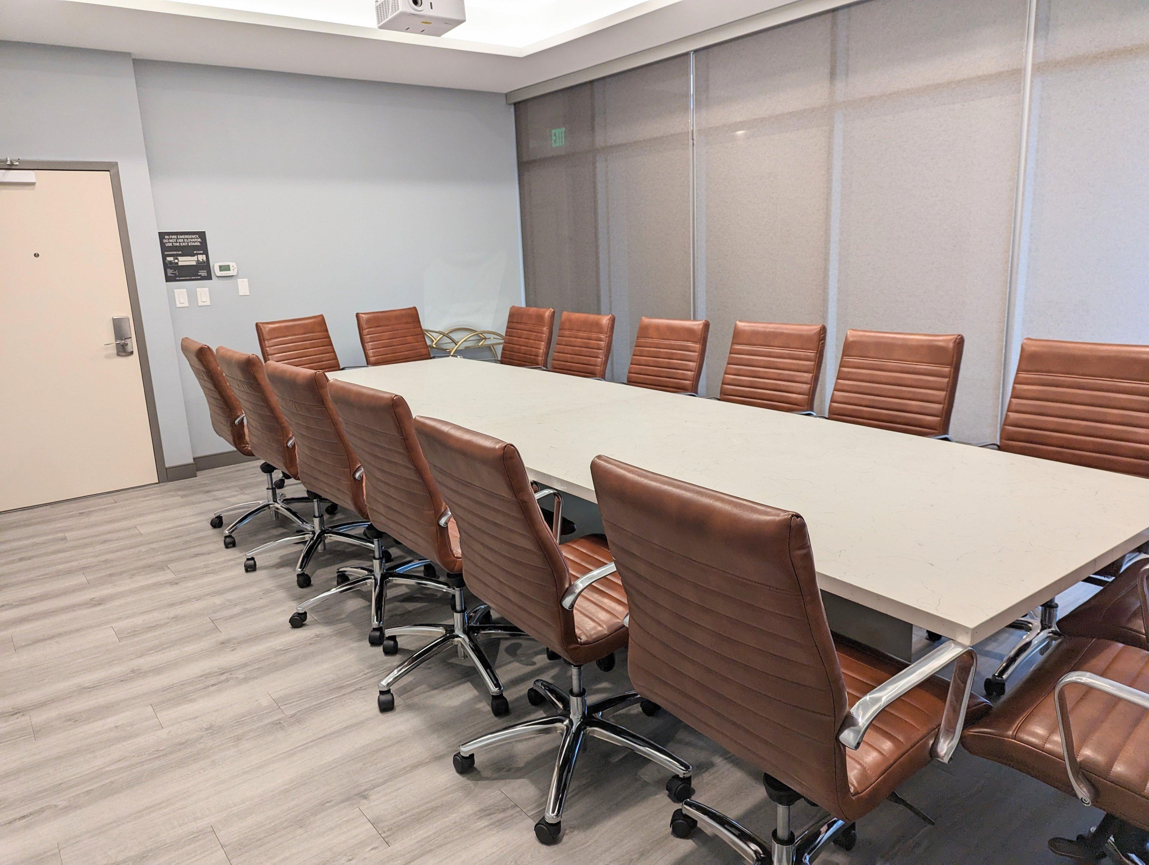 A conference room with a long table and eight brown leather chairs.