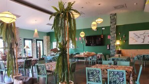 A restaurant with green walls, multiple tables and chairs, hanging lights, and potted plants.