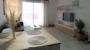 A modern living room with a dining table, sofa, TV, and decorative items.