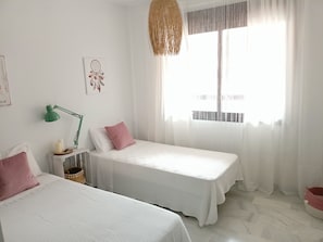 A bedroom with two beds, a green desk lamp, a dreamcatcher, and a window with sheer curtains. - Sea and Sun Golf Isla Canela-Costa Esuri (Ayamonte)