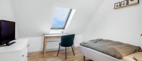 A bedroom with a skylight, a bed, a desk with a chair, and a TV on a dresser.
