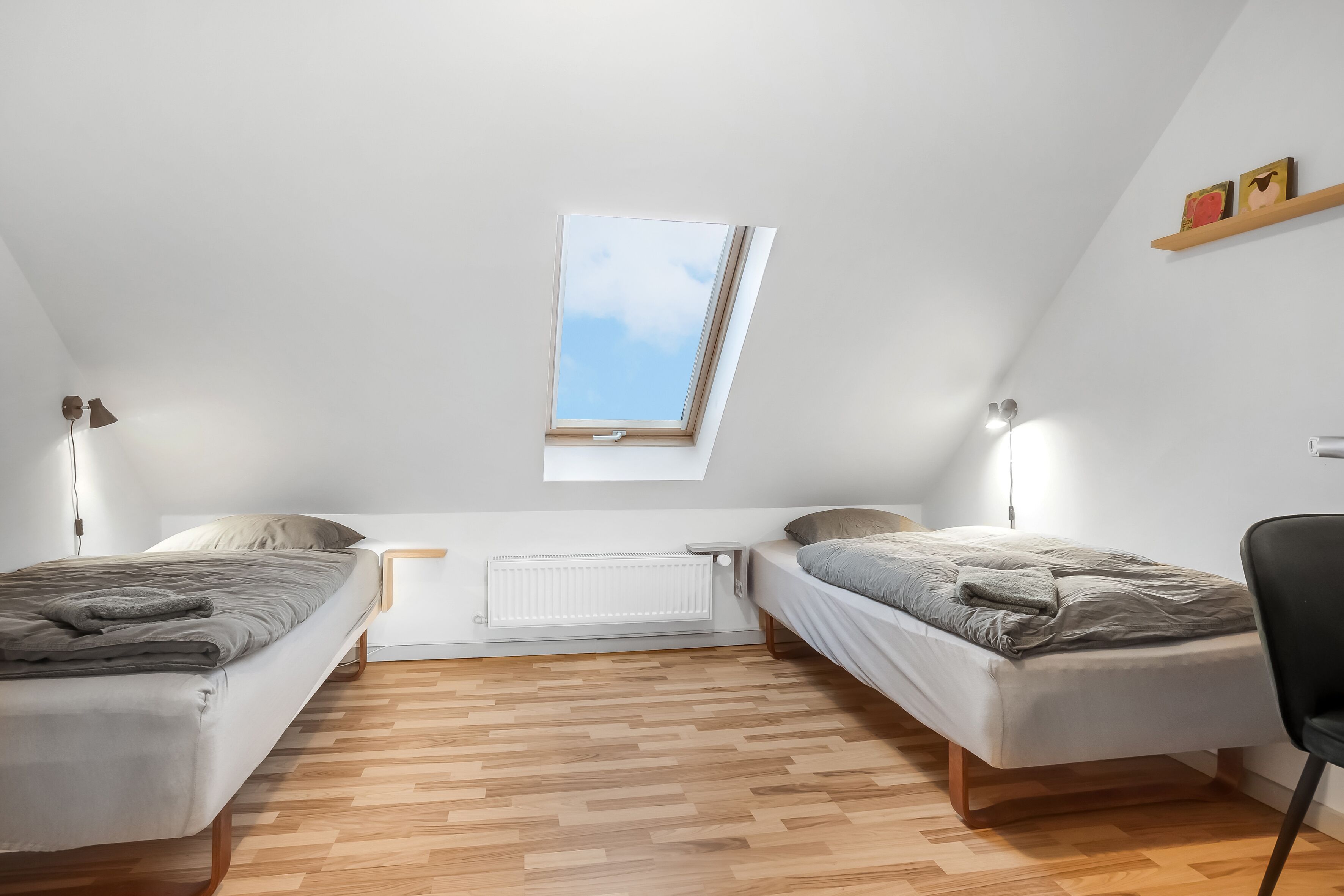 Un dormitorio pequeño y moderno con dos camas individuales, un tragaluz, un radiador y suelo de madera.