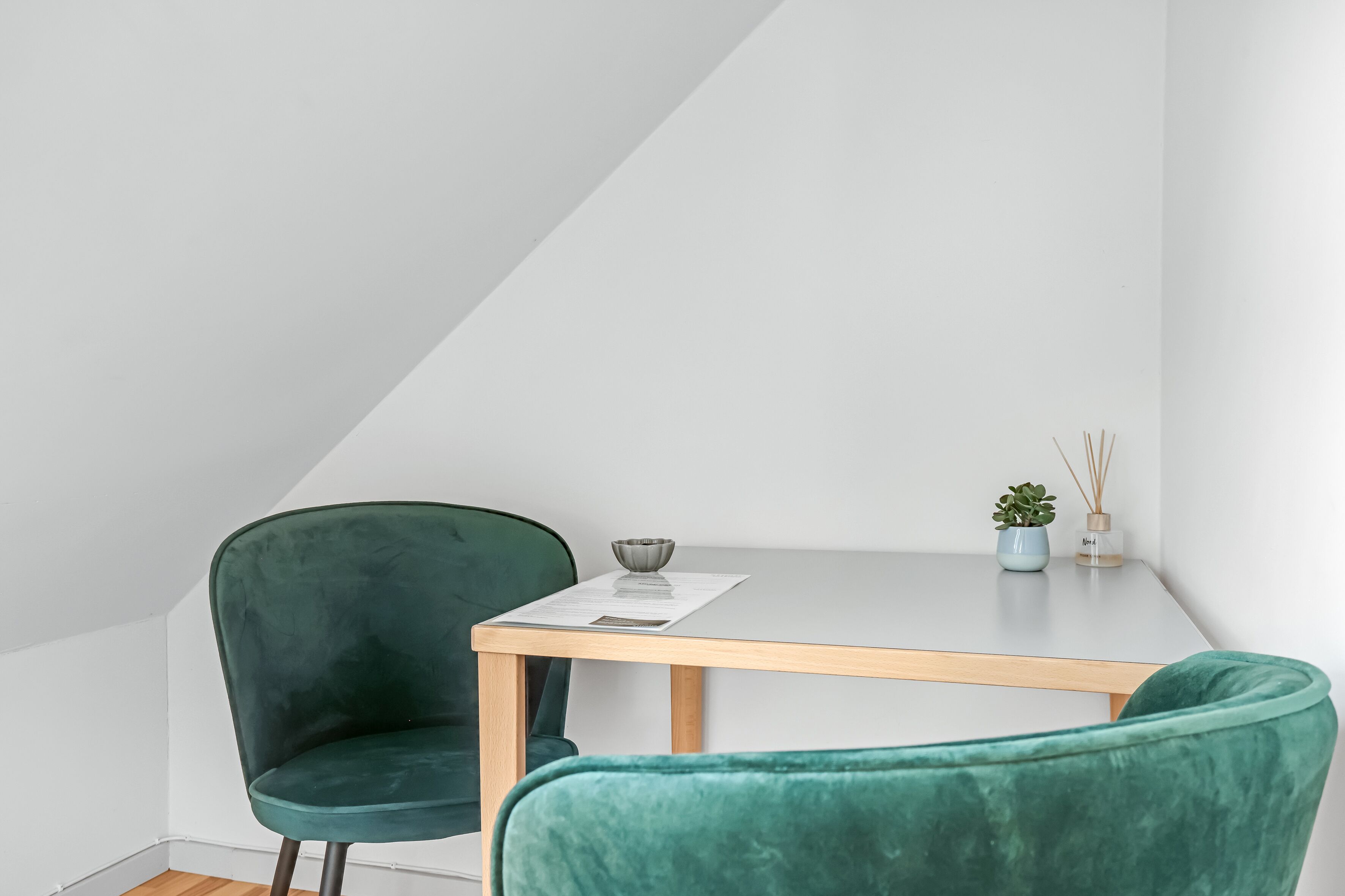 Habitación minimalista con una mesa de madera y dos sillas verdes.