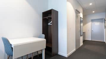 A room with a white desk, a blue chair, a dark wooden wardrobe, and a door with a sign.