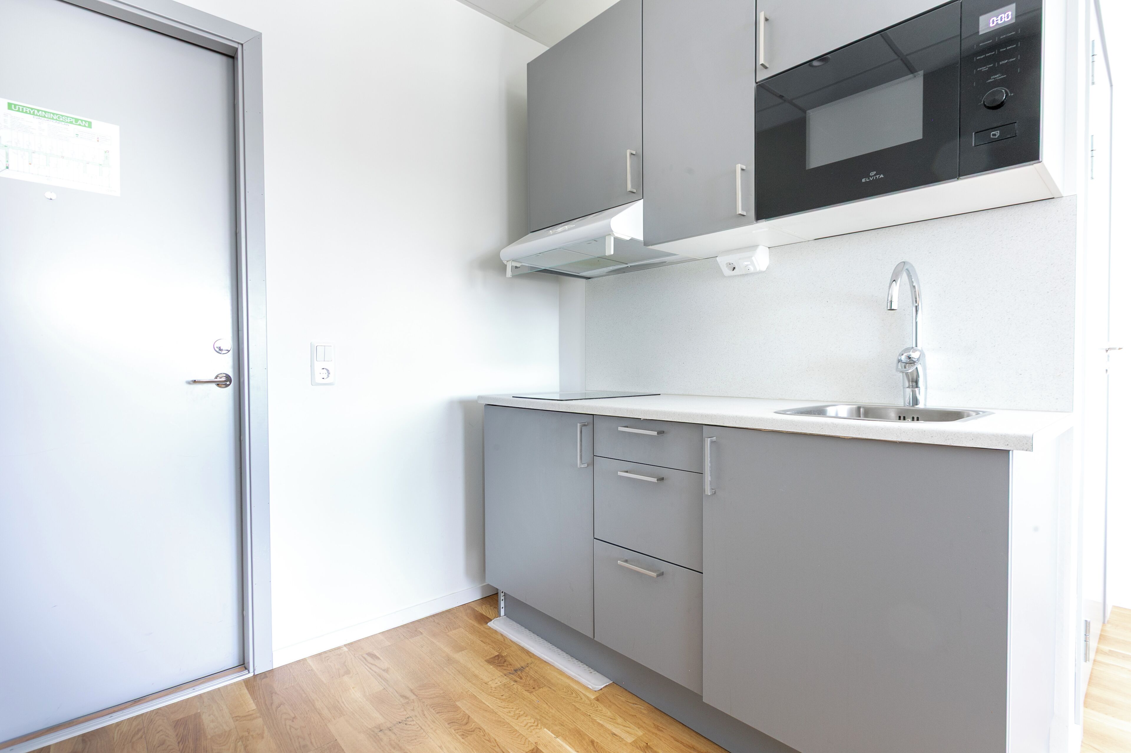 Una cocina con gabinetes grises, un lavamanos de acero inoxidable y un microondas negro.
