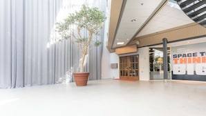 A modern interior with a large potted tree, a glass door entrance, and a sign reading "Explore Brändastad Space to Think Big". -  ApartDirect Arlandastad (Arlandastad)