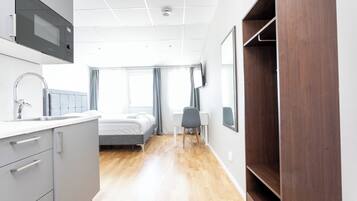 Una habitación de hotel moderna con kitchenette, una cama, un escritorio y un armario.