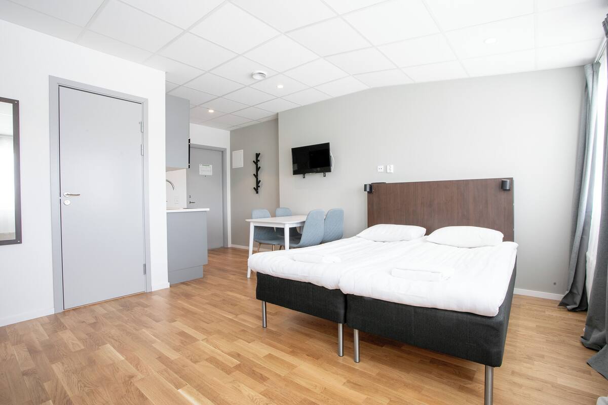 A modern hotel room with a double bed, a small table, a TV, and a bathroom visible through an open door.