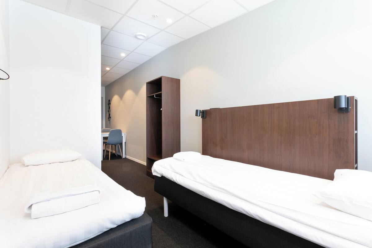 A hotel room with two single beds, a desk, and a chair.