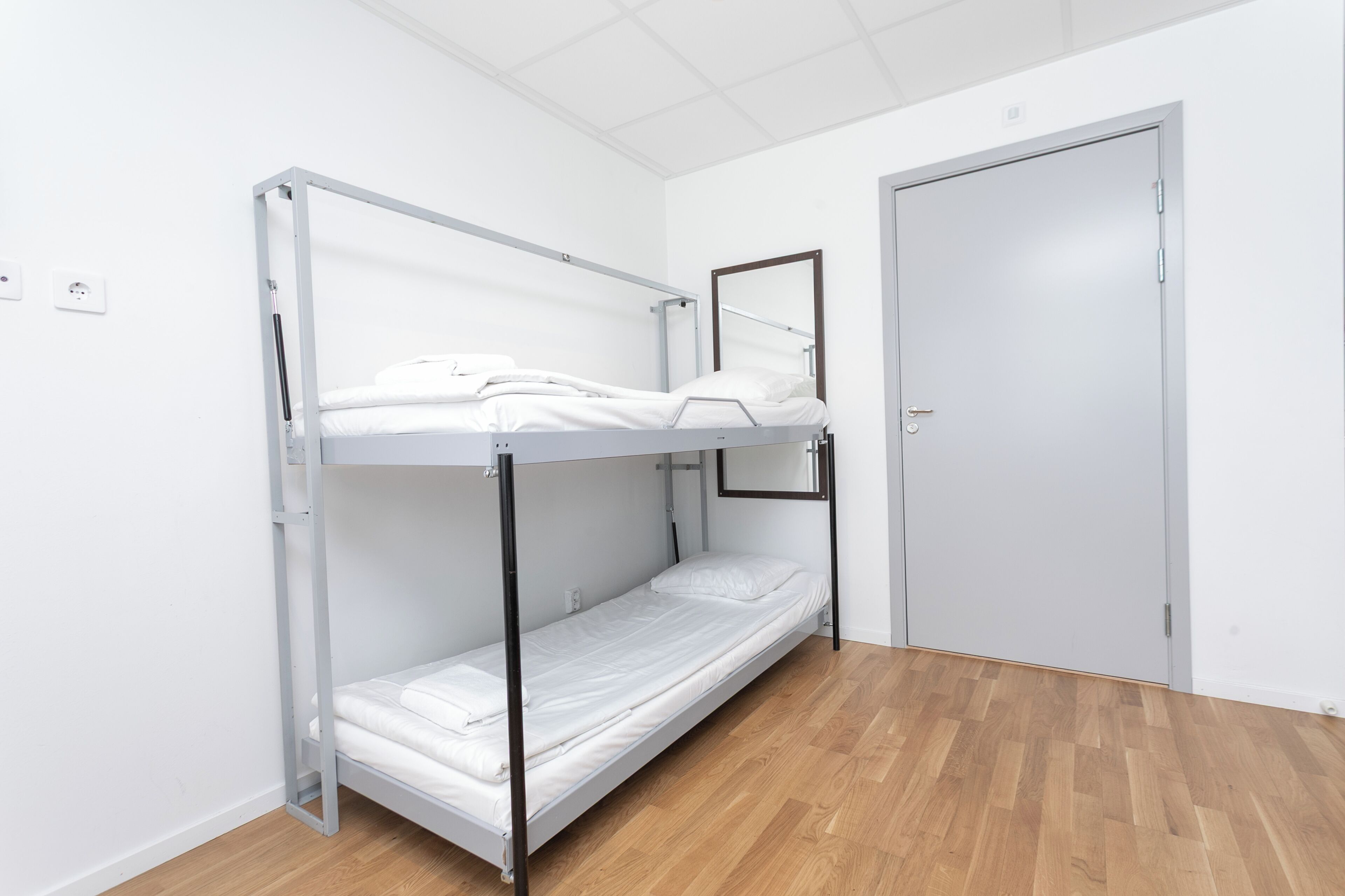 Una cama litera en una habitación con suelo de madera y una puerta cerrada.