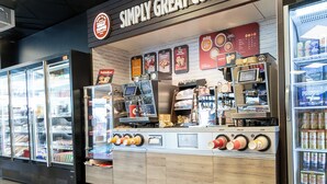A coffee shop with a coffee machine, menu boards, and refrigerated beverage dispensers. -  ApartDirect Arlandastad (Arlandastad)