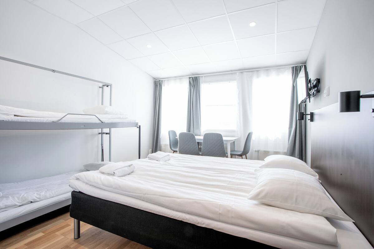 A hotel room with a bunk bed, a desk with chairs, and a large window with curtains.