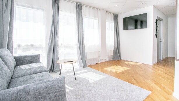 A modern living room with a grey sofa, a small round table, and sheer curtains. -  ApartDirect Arlandastad (Arlandastad)