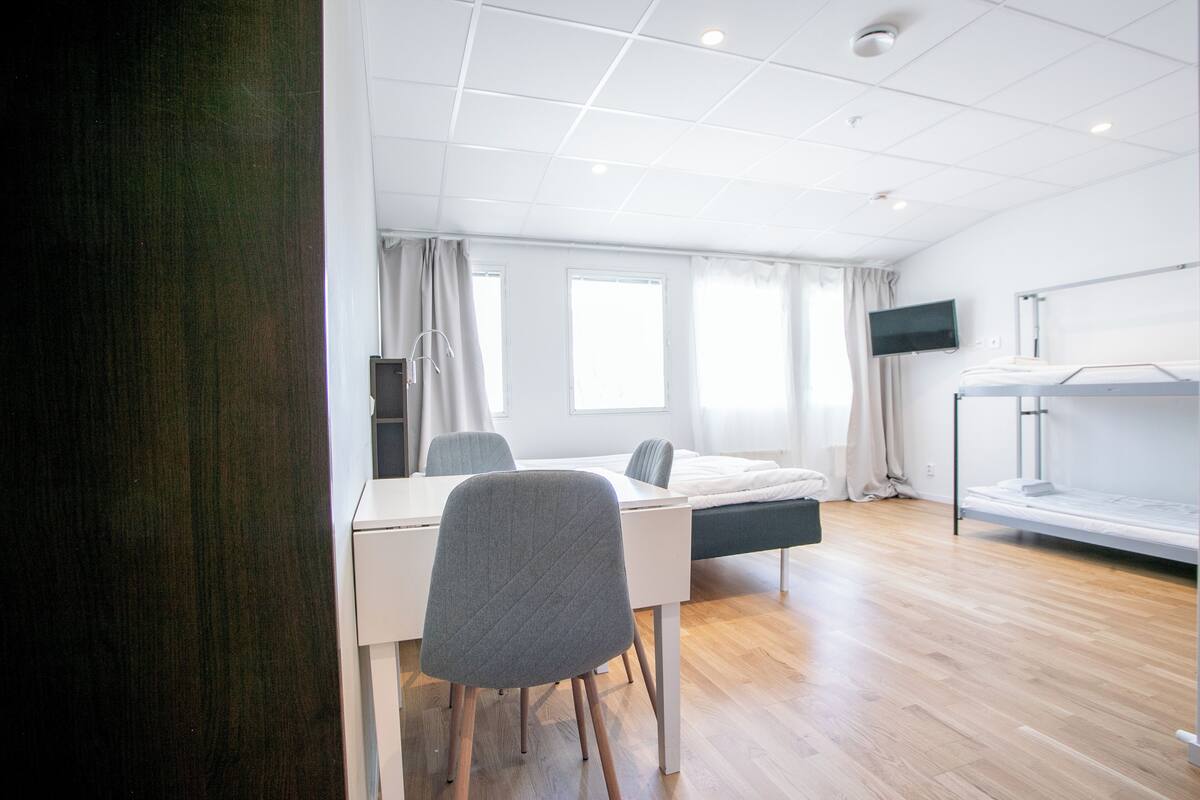 A modern hotel room with a bed, a desk, a chair, a TV, and a window.