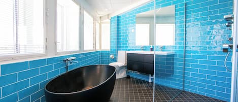 Un baño moderno con una bañera negra grande, cabina de ducha de vidrio y pared con azulejos azules.