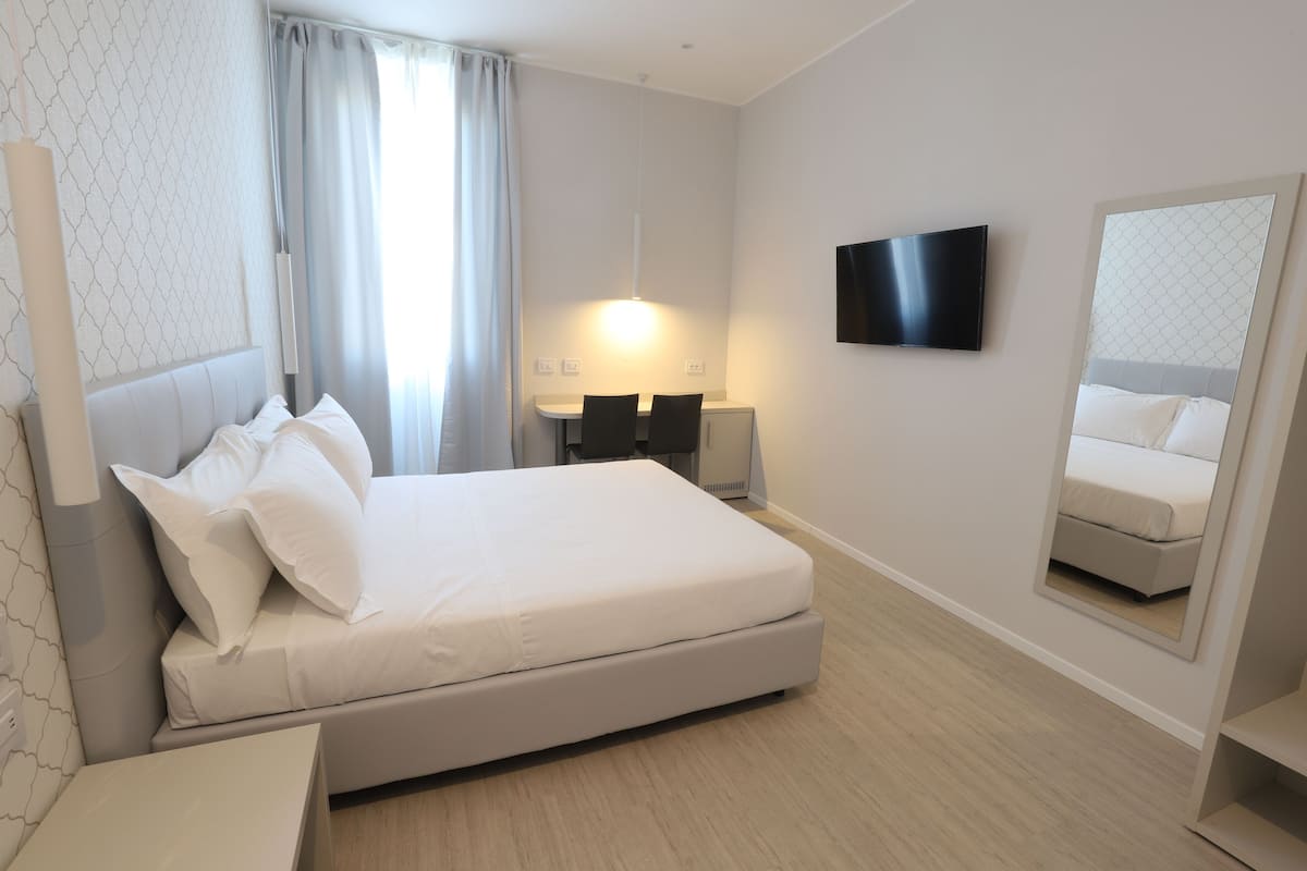 A modern hotel room with a large bed, a flat-screen TV, a bedside table, and a mirror.