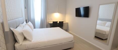 A modern hotel room with a large bed, a flat-screen TV, a bedside table, and a mirror.