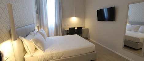 A modern hotel room with a large bed, a flat-screen TV, a bedside table, and a mirror.