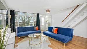 A modern living room with two blue sofas, a glass coffee table, and a white cowhide rug. - Cosy 3-Bedroom House • Free Parking • Garden • Fast Wifi • Self-Check-In (Coventry)