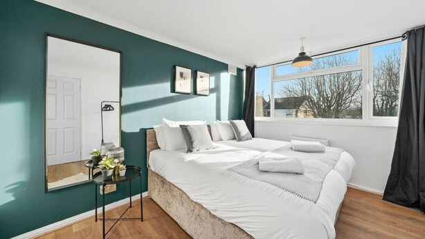 A bedroom with a large bed, a bedside table with a lamp, a mirror, and a window with curtains. - Cosy 3-Bedroom House • Free Parking • Garden • Fast Wifi • Self-Check-In (Coventry)